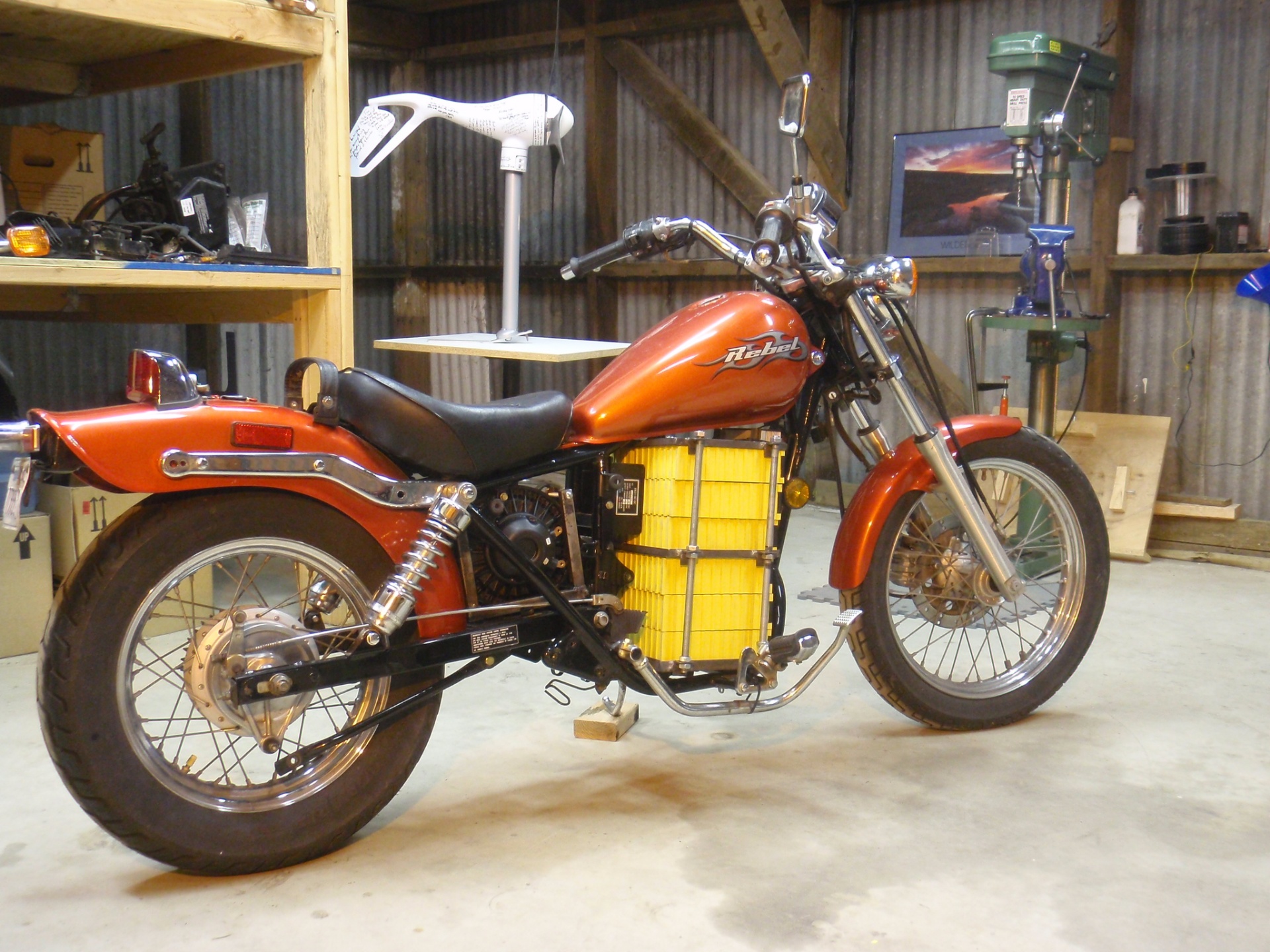 The finished custom electric Honda Rebel in the shop, orange tank and fenders with the yellow lithium battery pack mounted where the gas engine used to be