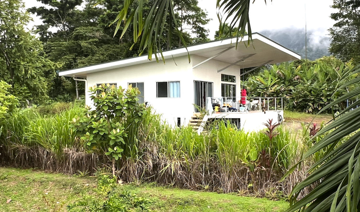 The finished white two-bedroom house in Ojochal, Costa Rica, set into the jungle with a wraparound deck and deep eaves